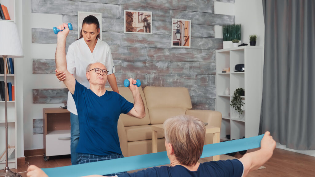 Une kinésithérapeute aide un couple de personnes âgées à faire des exercices de rééducation à domicile 