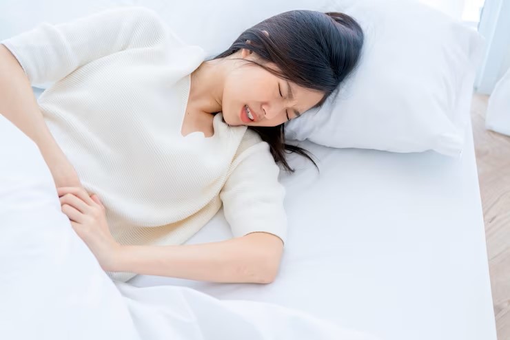 Photo d'une femme asiatique allongée dans son lit et ayant des douleurs menstruelles liées à l'endométriose